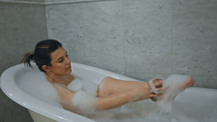 A relaxed young woman enjoys a bubble bath in a clean, modern bathroom setting.