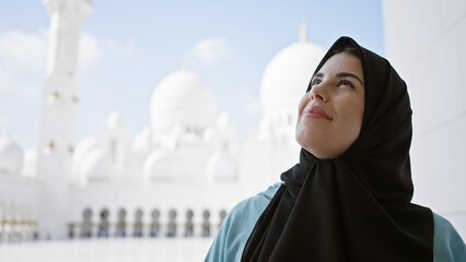 A young adult hispanic woman wearing a hijab looks contemplatively at the islamic architecture of a...