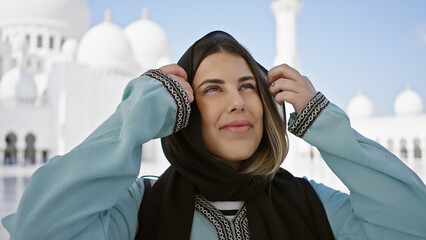 A smiling young woman wearing a hijab poses in front of the sheik zayed grand mosque in abu dhabi.