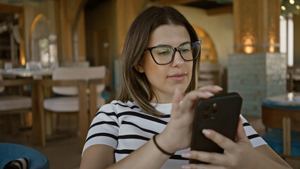 Young brunette woman using smartphone in a modern restaurant interior setting.