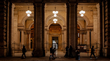 Crowd strolling at night near a grand building, illuminated by lights in Rome, Italy