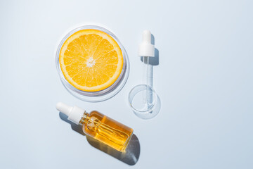 Bottle of cosmetic serum and petri dishes with orange fruit on blue background, flat lay. Space for...