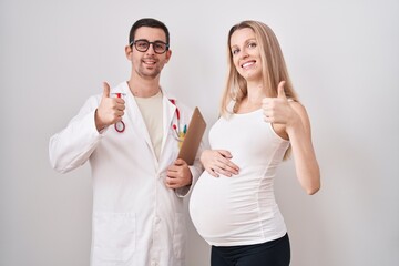 Young woman expecting a baby with doctor smiling happy and positive, thumb up doing excellent and approval sign