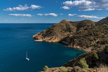 sailboat moored in a bay of the Serra Gelada Natural Park with the Albir Lighthouse in the background