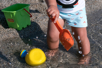 playing on the beach at the sunset time. baby playing with water on sea shore. closeup of the hand holding the watering can with water