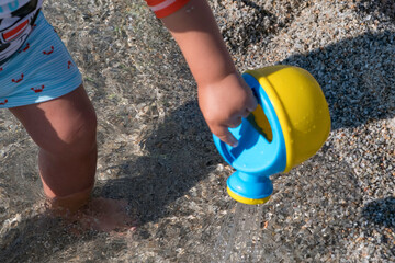 playing on the beach at the sunset time. baby playing with water on sea shore. closeup of the hand holding the watering can with water
