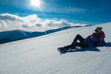 Woman in snowshoes lying in snow with view of mountains of Kor Alps, Lavanttal Alps, Carinthia...