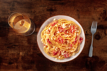 Carbonara pasta dish, traditional Italian spaghetti with pancetta and cheese, overhead flat lay shot with wine, on a dark rustic wooden background - 739966905