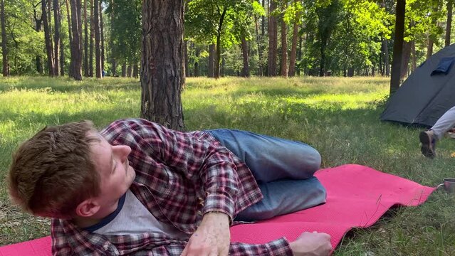 A family embarks on a delightful outdoor adventure. Bonding over the shared joy of camping at sunny day in the woods. Children mischievously play around, drawing on father face as he napping outdoors