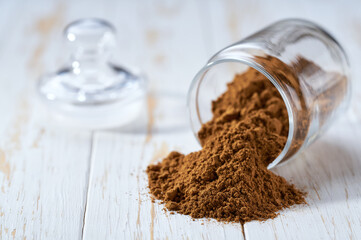 cinnamon powder poured out of a  storage jar on a white wooden table.