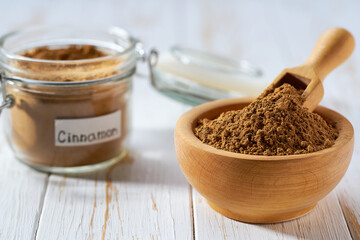 cinnamon powder in a wooden bowl  on a white wooden table, copy space for text.