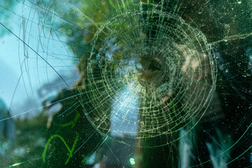 Close-up view of broken car window with trees reflected in background