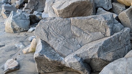 Granitic quarry rocks laid down along the shoreline for erosion control 50 years ago surrounded by polished river rocks all together in the mix at Swamis Reef Surf Park Encinitas California.