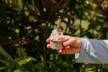 Birthday candle on a cupcake. Holiday concept. Man holding cake on background of plants