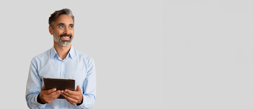 Smiling confident 40s latin hispanic mature business man holding digital tablet isolated on grey background. Older senior businessman, male leader professional using touchscreen pc. Banner, copy space