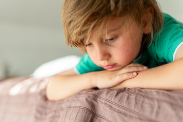 A thoughtful boy lies on the sofa . The child is sad alone at home. Childhood boredom and sadness...