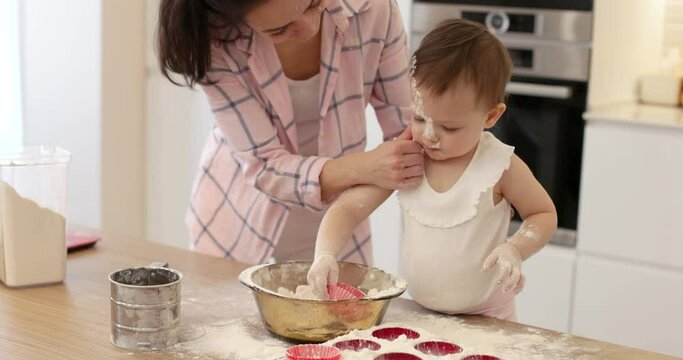 little baby girl is playing with flour in the kitchen. mom kiss her daughter