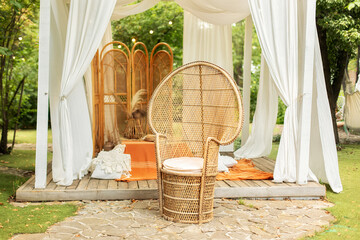 Rattan peacock armchair and decorative folding screen divider. Summer gazebo with flowing white curtains. Wedding boho decoration. Decor outdoor terrace with wicker furniture. Outdoor design of arbour © stock_studio