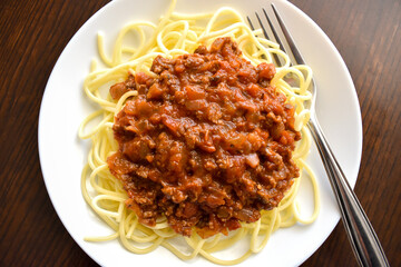 Spaghetti Bolognese with minced beef, onion, chopped tomato, garlic, olive oil, stock cube, tomato puree and Italian herb. Traditional Italian food with a fork on a white plate.