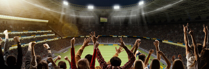 Back view of emotional football fans cheering favorite soccer team at crowded open air stadium at...