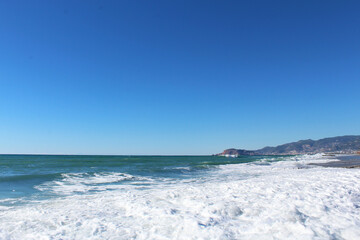 clear blue sky and waves with white foam at Mahmutlar beach in Turkey. mountains in the background