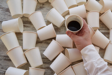 A businessman’s hand holding a cup with unfinished coffee over scattered cups on the table. Difficult decision, rush at work