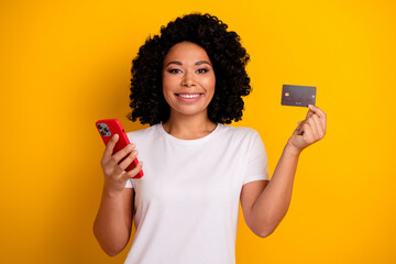 Portrait of charming attractive clever girl holding smartphone debit card recommend online payment isolated on yellow color background - obrazy, fototapety, plakaty