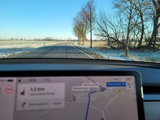 A shot on the move from behind the windshield of an electric car with snow-covered and iced fields. Cold sunny winter day. POV first person view shot on a iced plain road. Selective focus.
