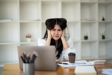 Young businesswoman stressed and having headache while working at desk with laptop in modern office