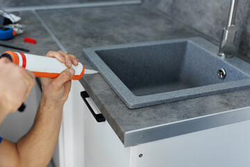 A worker seals up the kitchen sink with a sealant with a construction sealing gun.