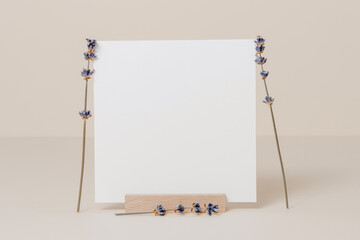 Empty minimal mockup paper card on wooden stand with lavender flowers, neutral aesthetic style....