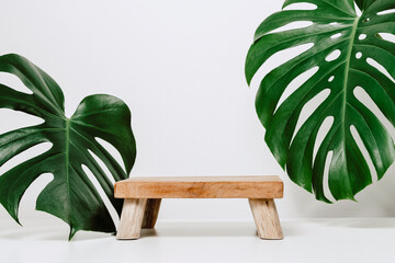 Wooden podium with copy space and natural monstera plant leaves on white background. Background for...