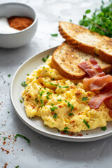 A breakfast serving of scrambled eggs, crispy bacon, and golden toast slices, on a light surface