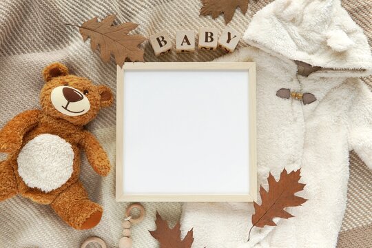 Pregnancy, baby coming announcement template, square wooden frame mockup for text, cozy fall flat lay composition with warm baby overalls, teddy bear toy, blanket, wooden letters, autumn leaves.