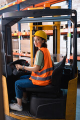 happy female forklift operator in hard hat and safety vest looking at camera in warehouse, logistics - 740018769