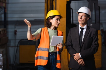 business meeting in a warehouse, female employee with tablet showing something to supervisor in suit