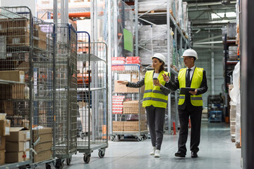 logistics team with hard hats walking with coffee near inventory while inspecting warehouse