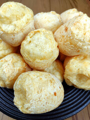 Closeup of a full plate with traditional brazilian cheese breads on the wooden table. Typical mining food, comida mineira or from Minas Gerais state.