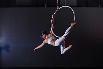 Poster Im Rahmen Young woman performing acrobatic element on aerial ring indoors © New Africa