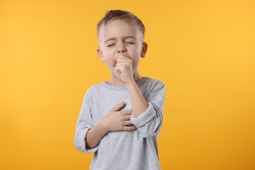 Sick boy coughing on yellow background. Cold symptoms