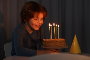 Cute boy with birthday cake at table indoors