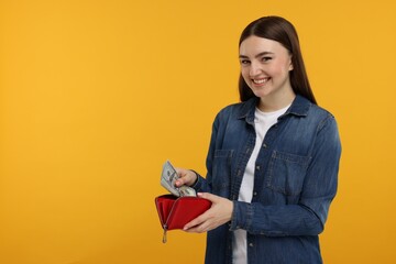 Happy woman putting money into wallet on orange background, space for text - obrazy, fototapety, plakaty