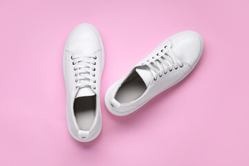 Pair of stylish white sneakers on pink background, top view