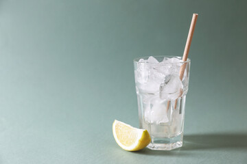 Refreshing drink with ice cubes in glass and lemon slice on light green background, closeup. Space for text