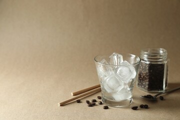 Cooking iced coffee. Ice cubes in glass, beans and straws on beige background. Space for text