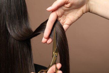 Hairdresser cutting client's hair with scissors on light brown background, closeup