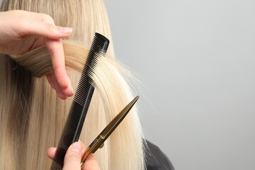 Hairdresser combing and cutting client's hair on light grey background, closeup. Space for text