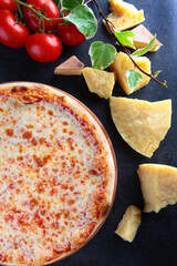 Pizza Margarita. Classic pizza. Hard cheese and cherry tomatoes on a dark background. View from...