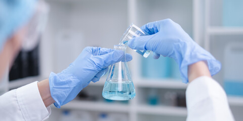 Close-up hands holding pouring blue fluid liquid beaker flask test tube glassware sample laboratory...