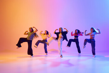 Dynamic image of talented, artistic teen girls dancing hip hop against gradient studio background in neon light. Concept of hobby, youth, childhood, style, fashion, dance school - obrazy, fototapety, plakaty